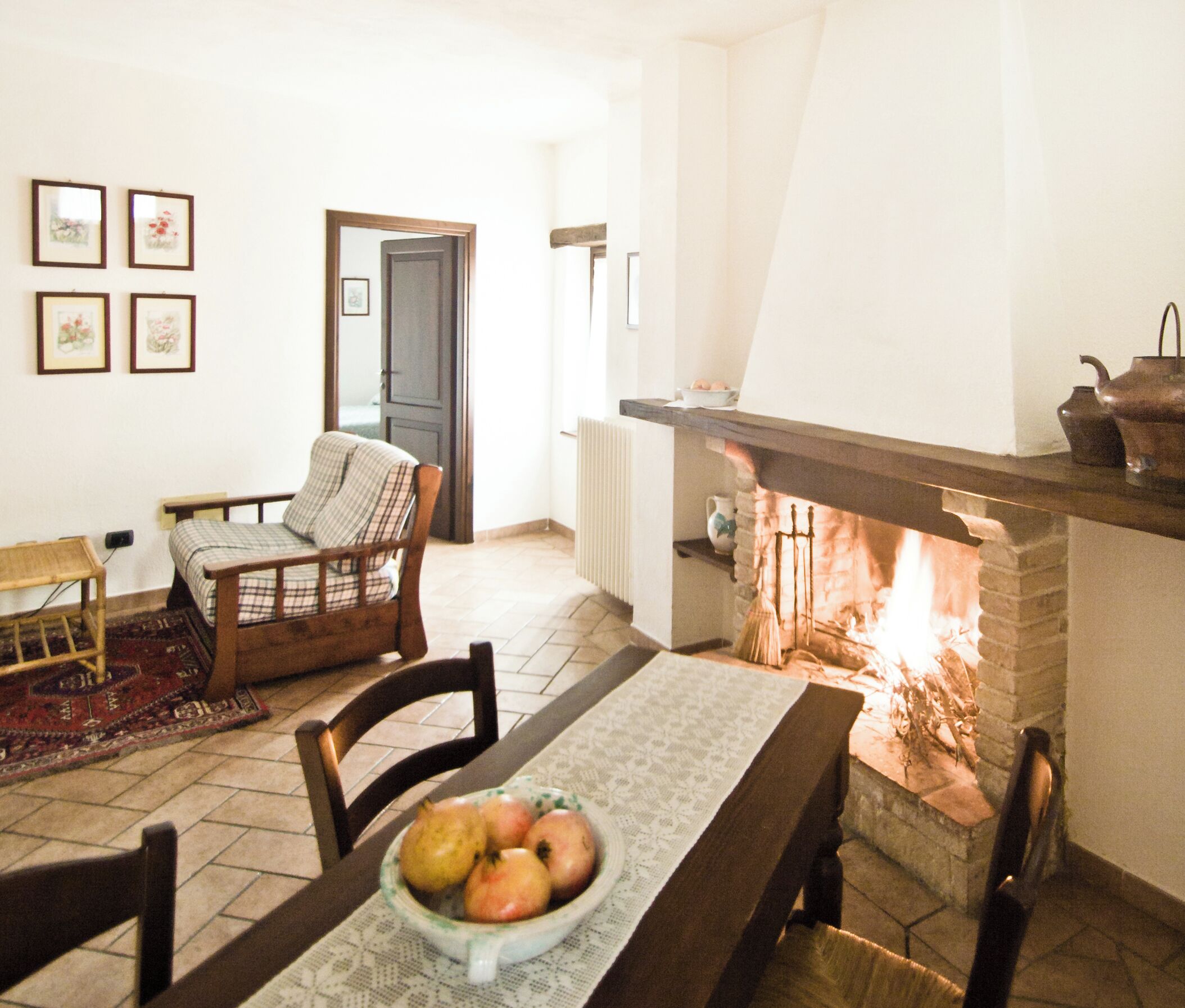 A cozy living room with a fireplace, a dining table with a bowl of fruit, and a chair.