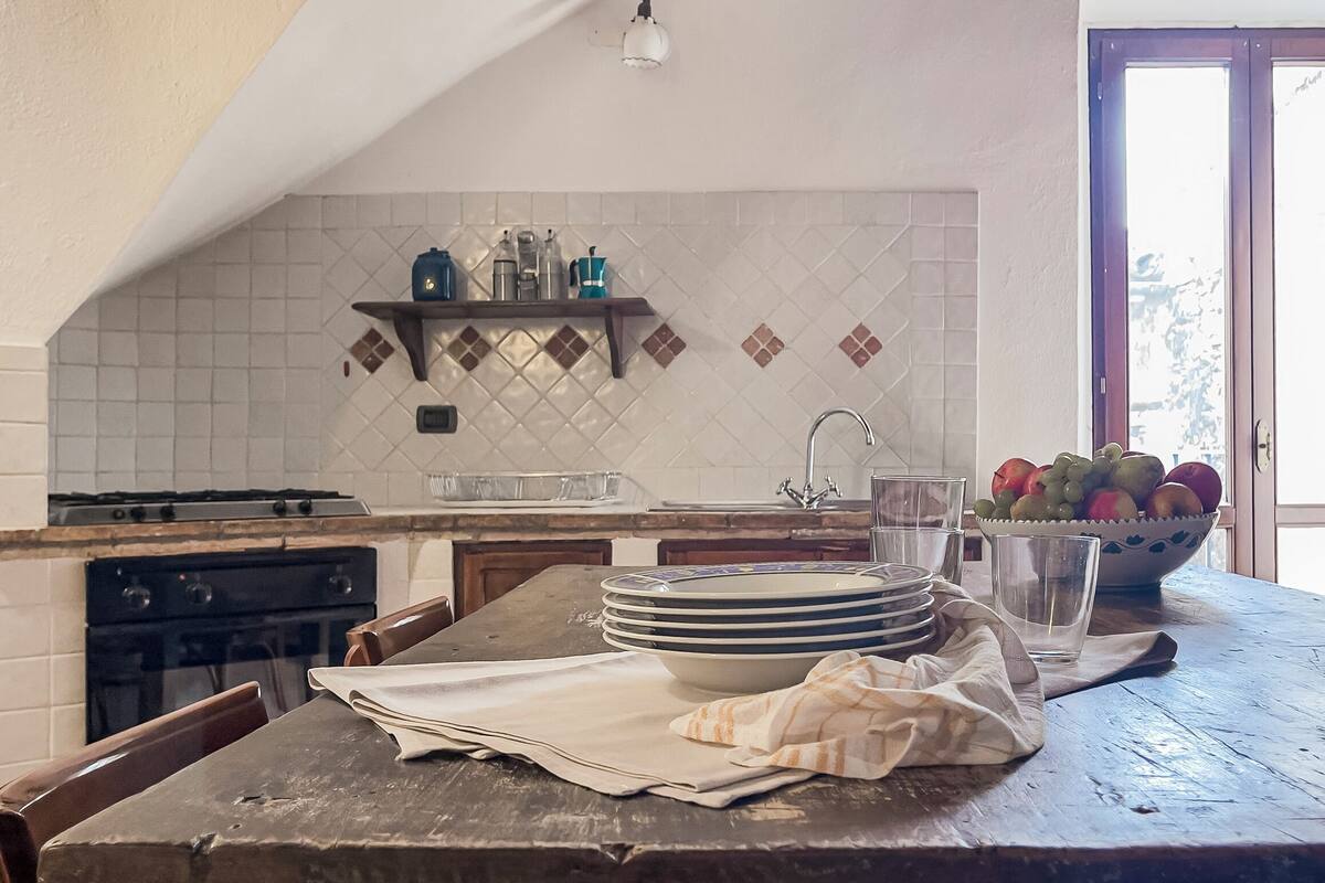 A kitchen with a tiled backsplash, a stove, a sink, and a window with a view.