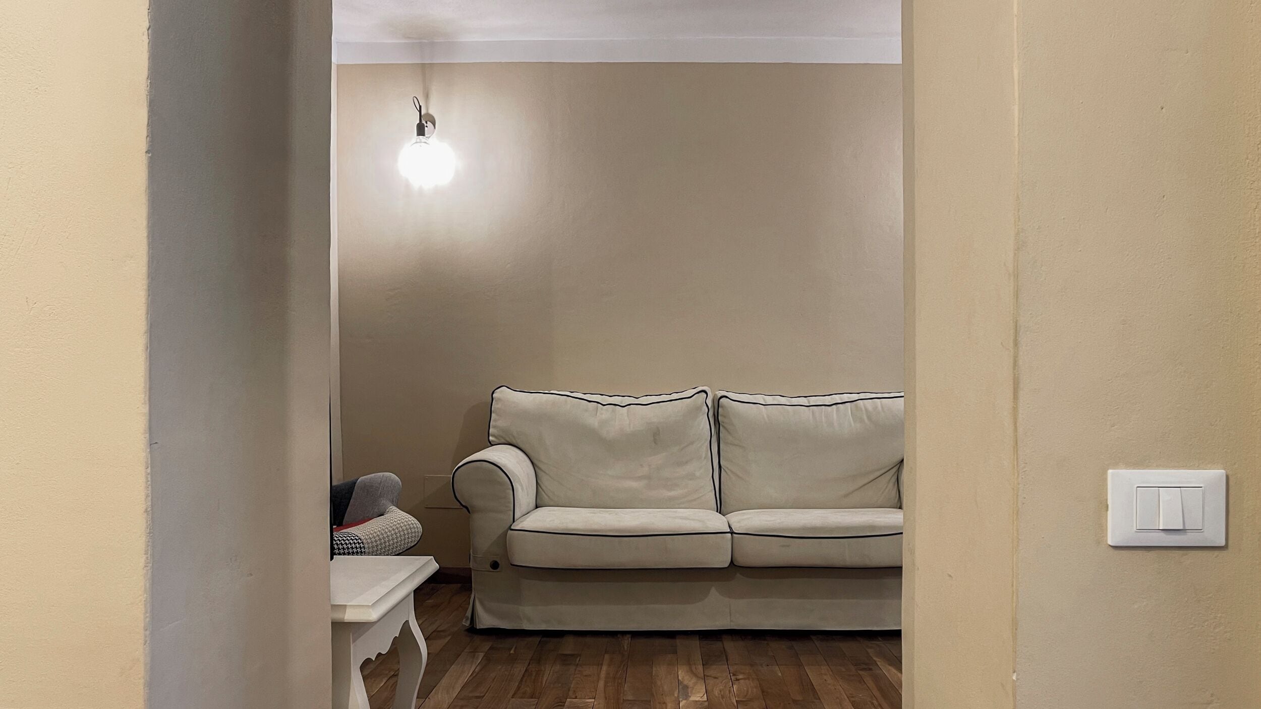 Ein Zimmer mit einer beigen Wand, einem weißen Tisch, einem beigen Sofa und einer Deckenleuchte.