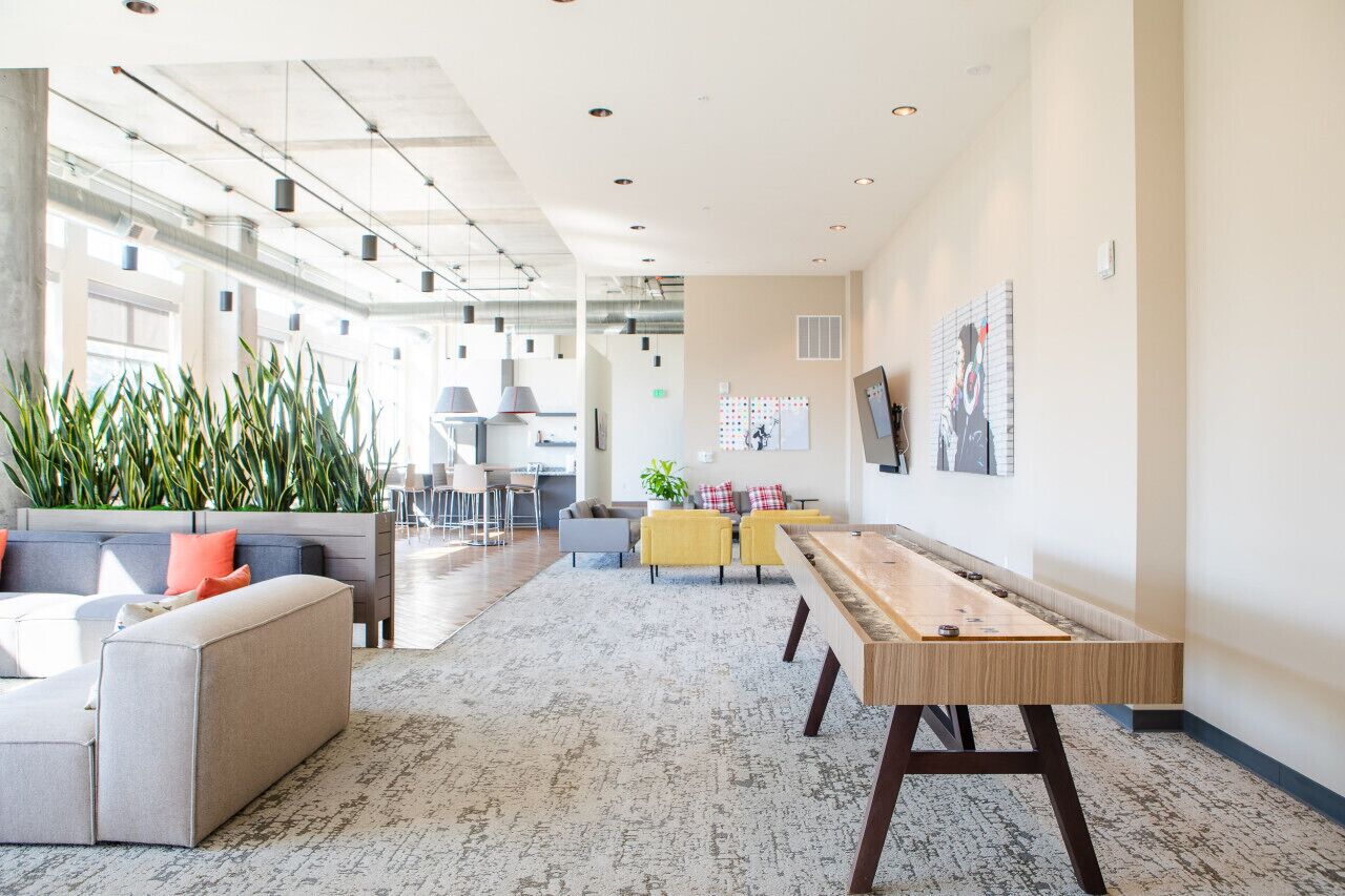 A spacious, well-lit lounge area with a long table, comfortable seating, and large windows allowing natural light.