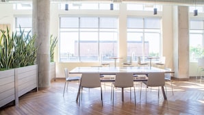 A spacious conference room with a large table and chairs, large windows, and potted plants.