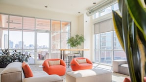 A spacious, modern lounge with large windows offering a city view, comfortable seating, and a central table.