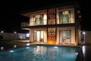 Een modern huis met twee verdiepingen en een zwembad op de voorgrond.