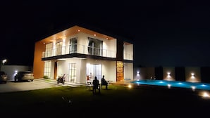 A modern two-story house with a swimming pool, large windows, and a well-lit exterior.