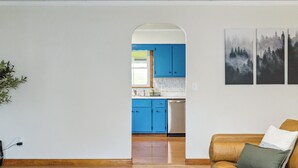 A living room with a sofa and a coffee table, a kitchen with blue cabinets, and a dining area with a table and chairs. - Charming Catskill getaway walking distance to Main St. Pet-friendly! (Catskill)