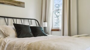 A neatly made bed with a white comforter and two pillows, a bedside lamp, and a window with curtains. - Charming Catskill getaway walking distance to Main St. Pet-friendly! (Catskill)