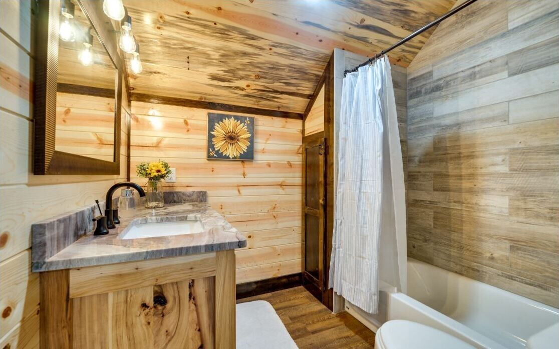 Un baño de cabaña de madera con lavamanos, espejo y ducha.