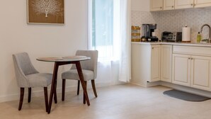 A dining area with two chairs, a round table, a coffee machine, and a kitchen counter with cabinets. - Large, Newly Built 1B Studio w/ Patio, W&D (Naples)