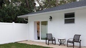 A white house with a covered patio, two chairs, and a small table. - Large, Newly Built 1B Studio w/ Patio, W&D (Naples)