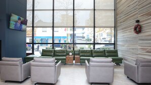 A modern lobby with a large window, green sofas, and a flat-screen TV on the wall. - Hotel Partner & Spa (Vlorë)