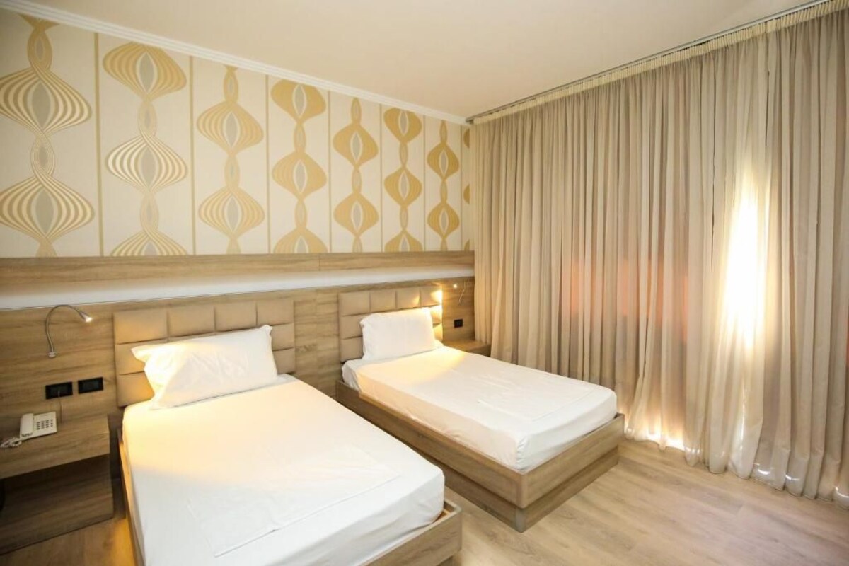 Camera d'albergo con due letti, una testiera in legno, una parete decorata e una tenda.