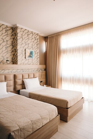 A hotel room with two beds, a stone-patterned wall, a framed picture, and a large window with curtains. - Hotel Partner & Spa (Vlorë)