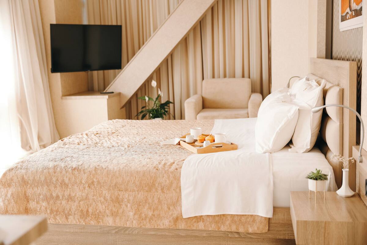A neatly arranged bedroom with a bed, a bedside table, a chair, a TV mounted on the wall, and a staircase.
