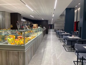 A modern restaurant with a glass display case filled with fruits and a seating area with tables and chairs. - Hotel Partner & Spa (Vlorë)