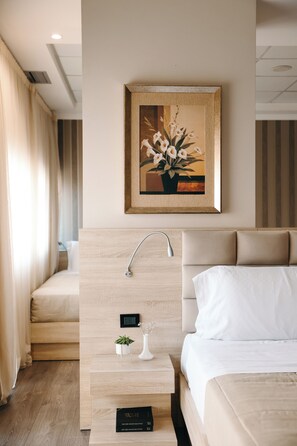 A modern hotel room with a wooden headboard, a bedside table with a small plant, a framed artwork above the bed, and a control panel on the wall. - Hotel Partner & Spa (Vlorë)