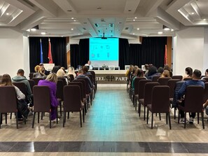A conference room with rows of chairs facing a stage with a presentation screen. - Hotel Partner & Spa (Vlorë)