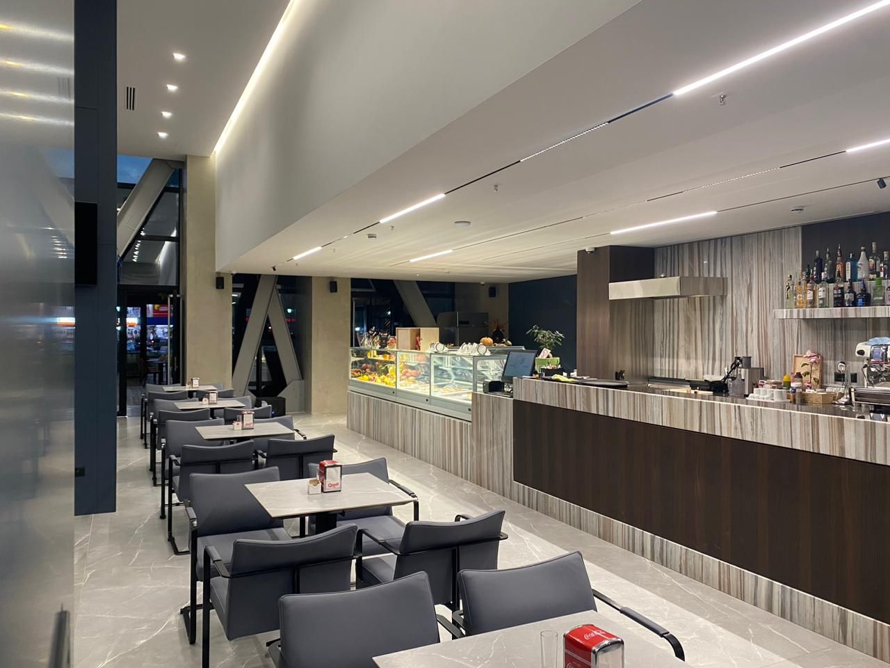 A modern restaurant with a long counter, seating area, and a display case with food items.
