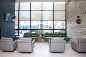 A modern lobby with a large window, green sofas, and a flat-screen TV on the wall. - Hotel Partner & Spa (Vlorë)