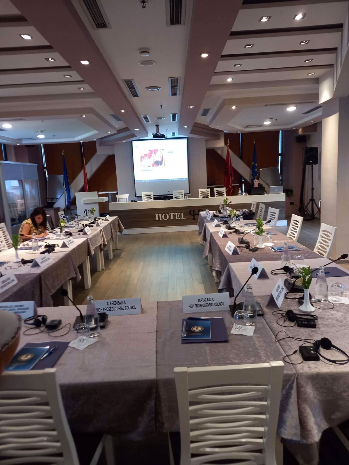 A conference room with long tables, nameplates, and a large screen at the front.