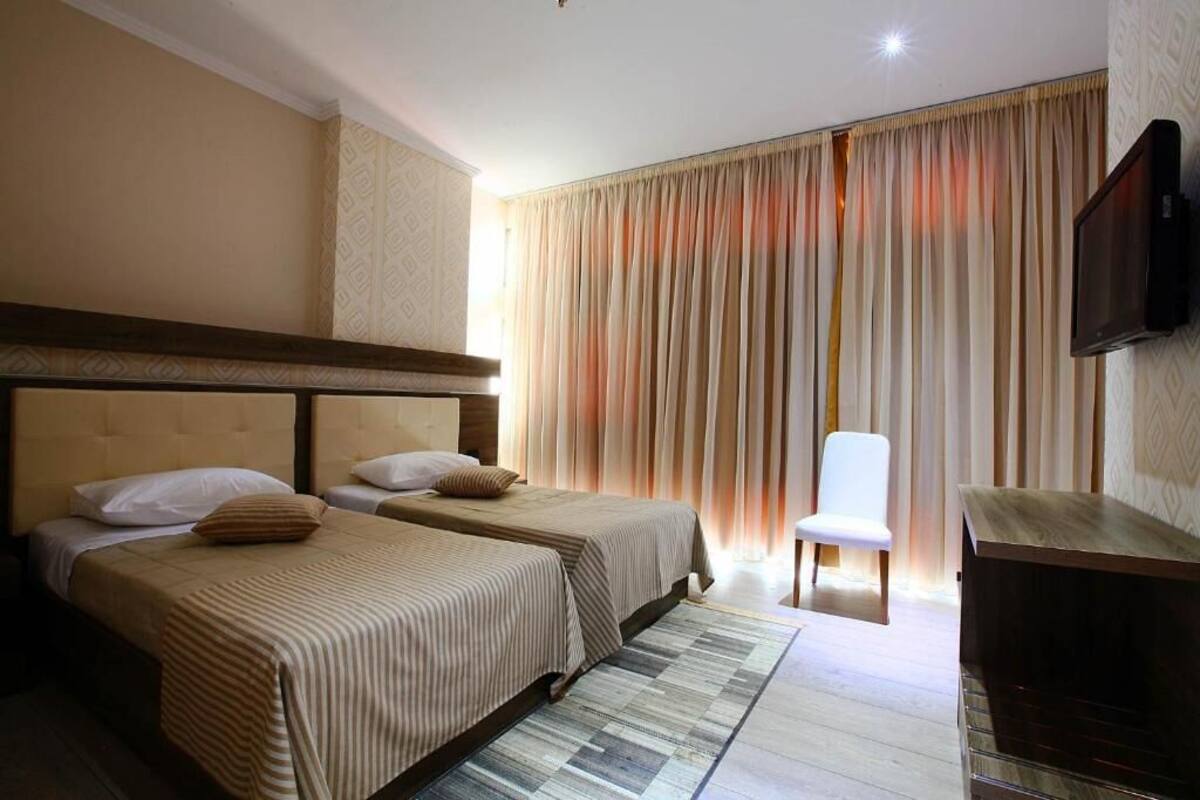 A hotel room with two beds, a TV, a chair, and a wooden cabinet.