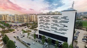 A modern building with a unique facade, surrounded by a parking area and a roundabout. - Hotel Partner & Spa (Vlorë)