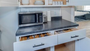 A compact kitchen with white cabinetry, a microwave, a toaster, and a drawer with utensils.