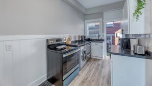 A modern kitchen with white cabinets, stainless steel appliances, and a wooden floor.