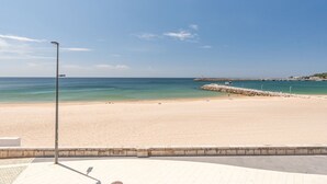 Ein Strand mit einem gepflasterten Weg, einem Steg und blauem Himmel.