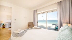 Ein Hotelzimmer mit einem großen Bett, einem Sessel, einem Schreibtisch und Blick auf den Strand.