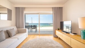 Ein modernes Hotelzimmer mit Sofa, Fernseher, Schreibtisch und Blick auf den Strand.