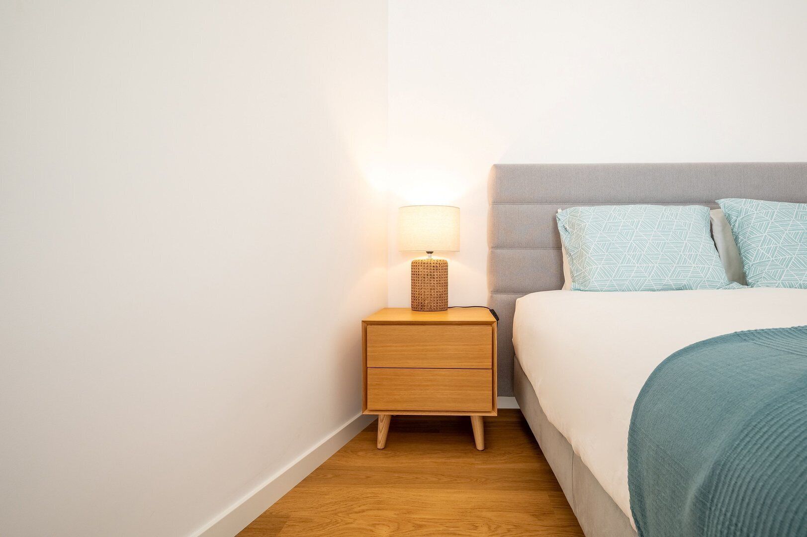 Une chambre à coucher bien rangée, avec un lit, une table de chevet dotée d’une lampe et une petite table de nuit.