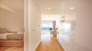 A modern hotel room with a bed, a small desk, and a view of the sea.