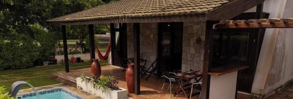 Un espacio al aire libre techado con piscina, paredes de piedra y mobiliario exterior.
