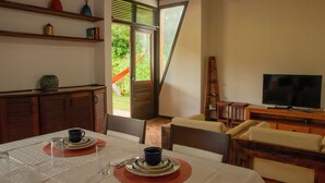 A dining area with a table set for two, a television, and a view of the outdoors. - Casa Pipa Natureza Piscina Privativa 089 (Tibau do Sul)