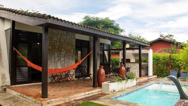 A covered patio with a pool, stone walls, and outdoor furniture. - Casa Pipa Natureza Piscina Privativa 089 (Tibau do Sul)