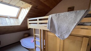 A room with a sloped ceiling, a bunk bed with a grey blanket, a wooden cabinet, and a skylight. - Wifi, 1st floor, balcony, tv, ski locker, 34m², Serre Chevalier (Le Monêtier-les-Bains)