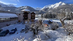 A snow-covered courtyard with a building, parked cars, and snow-covered trees. - Wifi, 1st floor, balcony, tv, ski locker, 34m², Serre Chevalier (Le Monêtier-les-Bains)