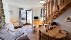 A cozy living room with a sofa, a wooden dining table with cups, a small side table, and a staircase. - Wifi, 1st floor, balcony, tv, ski locker, 34m², Serre Chevalier (Le Monêtier-les-Bains)