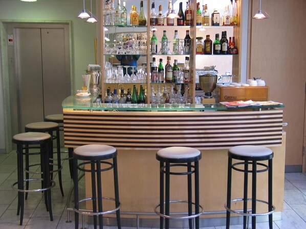 Una zona de bar con una barra de cristal, varios taburetes y estantes llenos de botellas de licor.
