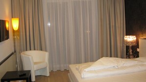A hotel room with a bed, a chair, a small table, and a lamp. - City Hotel (Linz)
