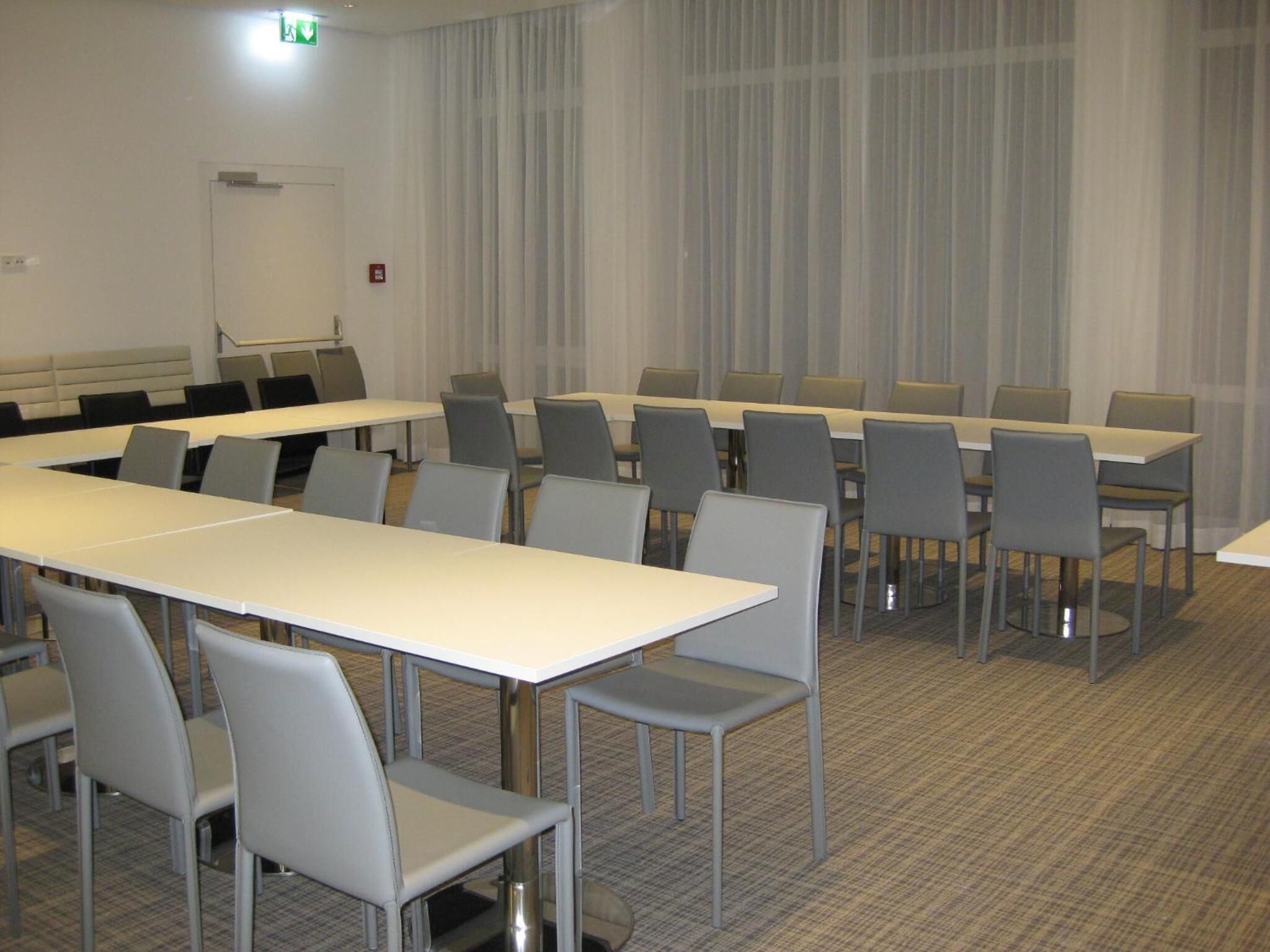 A conference room with multiple tables and chairs, a whiteboard, and a fire alarm on the wall.