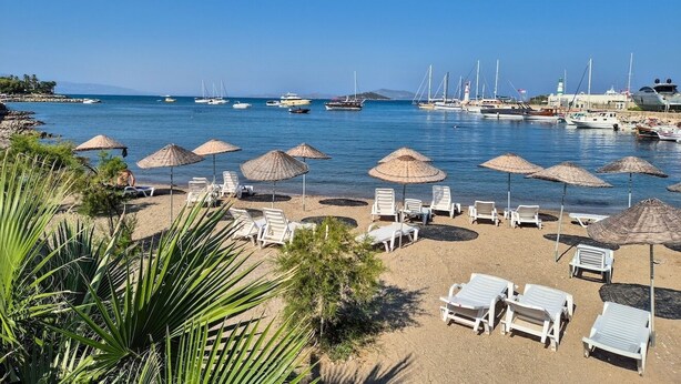 A beach with sun loungers and umbrellas, boats in the water, and a clear sky. - Suelo Flat Villa for Family (Bodrum)