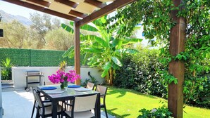 An outdoor patio with a table and chairs, a grill, and lush greenery. - Suelo Flat Villa for Family (Bodrum)