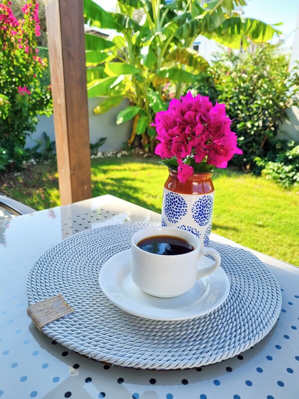 A white cup of coffee on a white saucer with a blue pattern, placed on a round table with a woven edge.