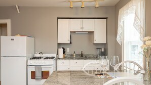 Une cuisine moderne avec des meubles blancs, un plan de travail en granit et un coin repas comprenant une table et des chaises.