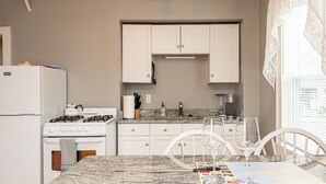 Une cuisine compacte avec des meubles blancs, une cuisinière à gaz, un réfrigérateur et un coin repas comprenant une table et des chaises.