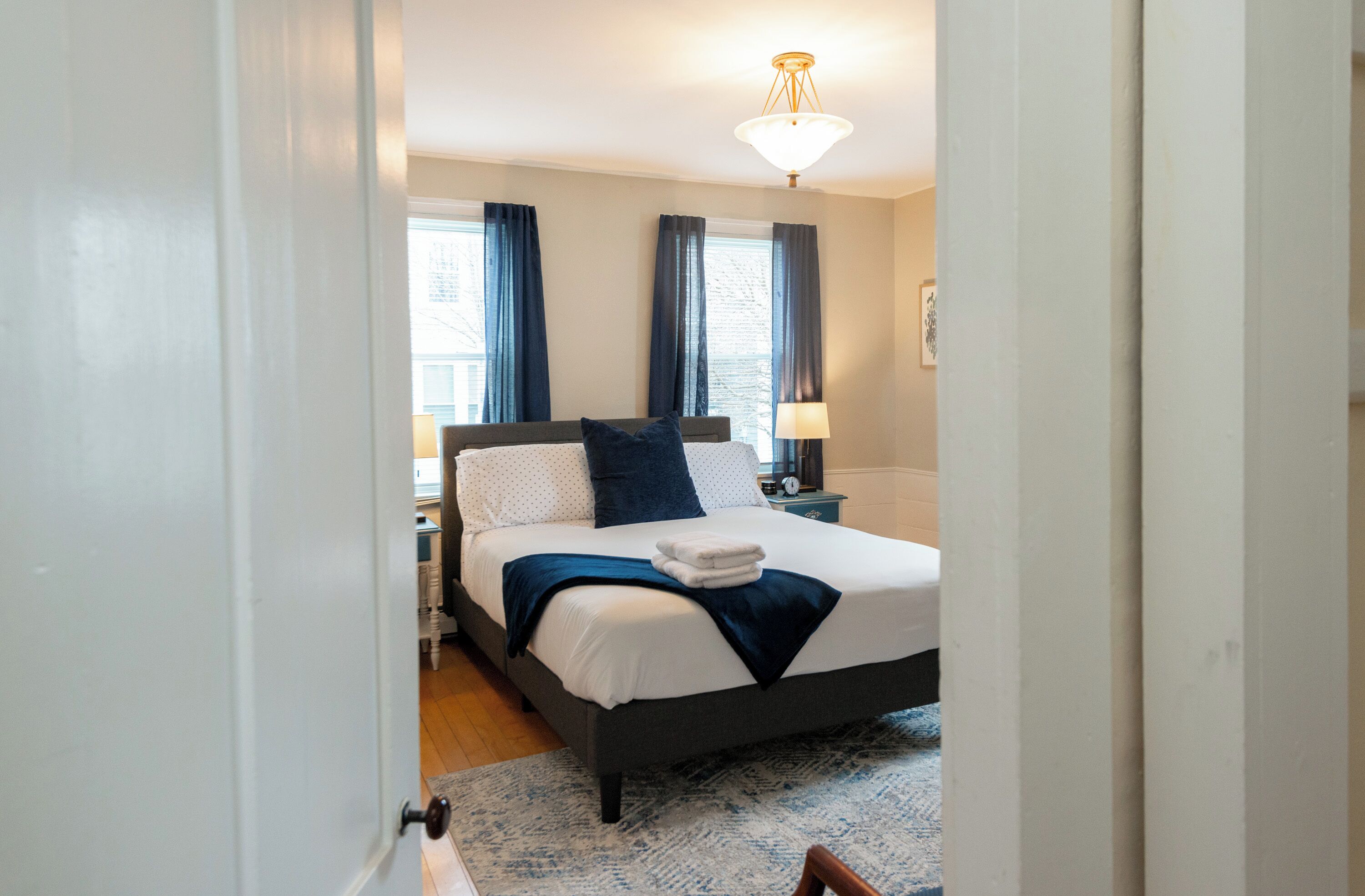 Un dormitorio con una cama, mesitas de noche, una lámpara y una ventana con cortinas.
