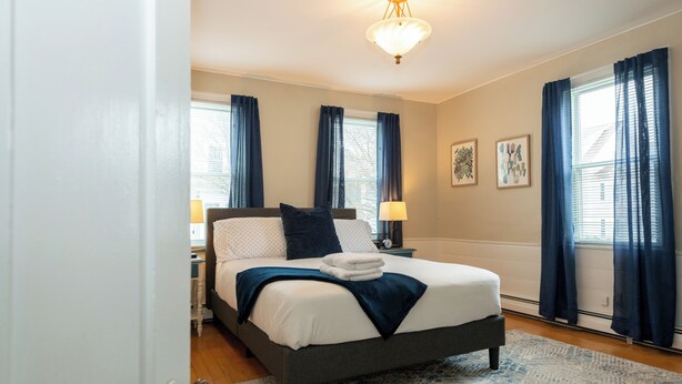 Un lit bien fait, avec une tête de lit grise, une lampe de chevet et un tapis aux motifs bleus et blancs.