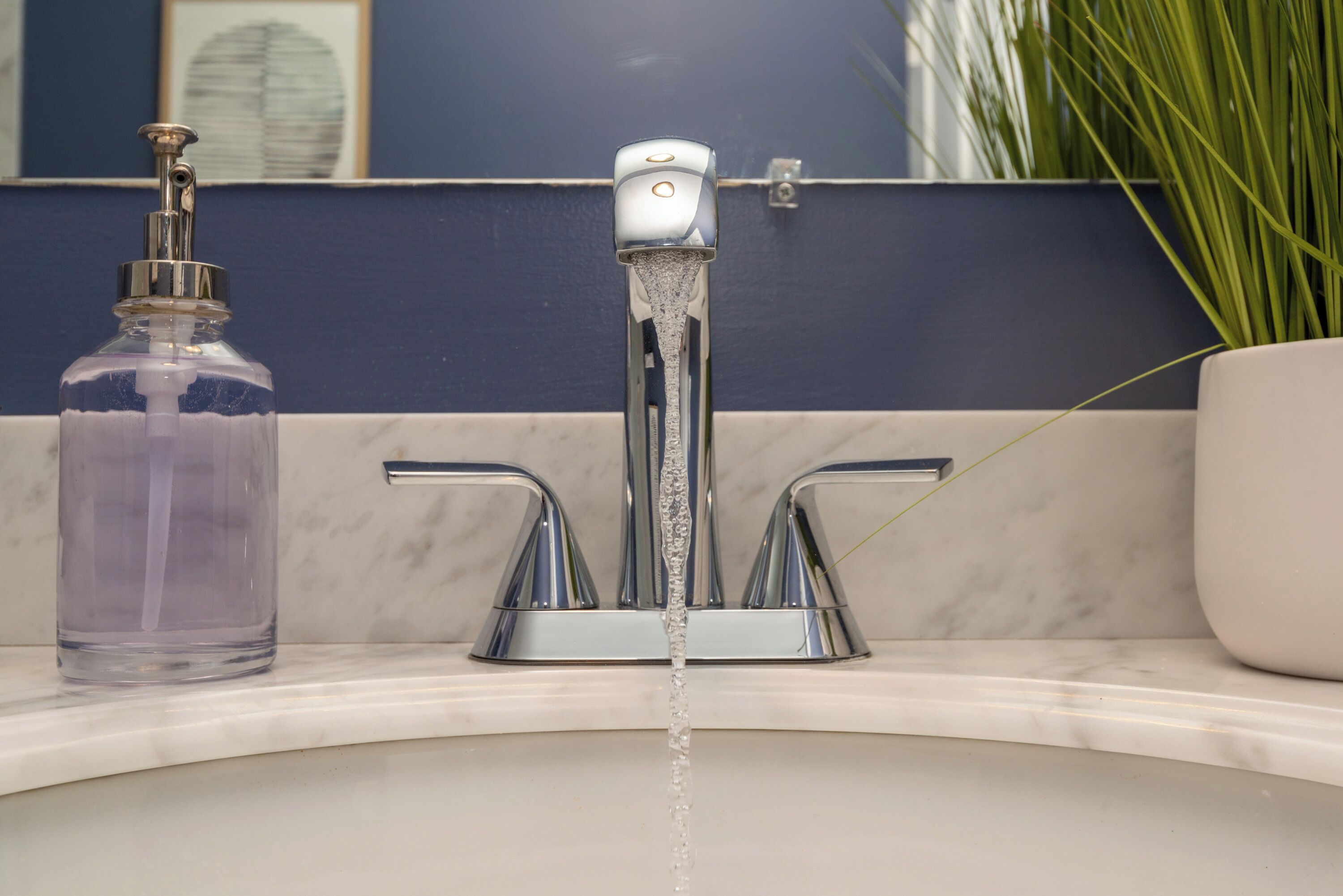 A bathroom with a modern faucet, a clear glass soap dispenser, and a marble countertop.