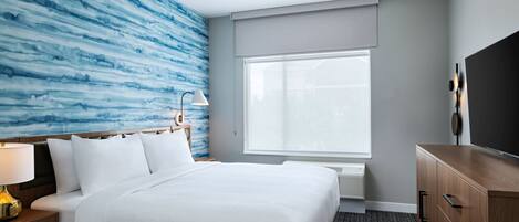 Une chambre d’hôtel avec un lit, une table de chevet, une lampe, une commode et une grande fenêtre.